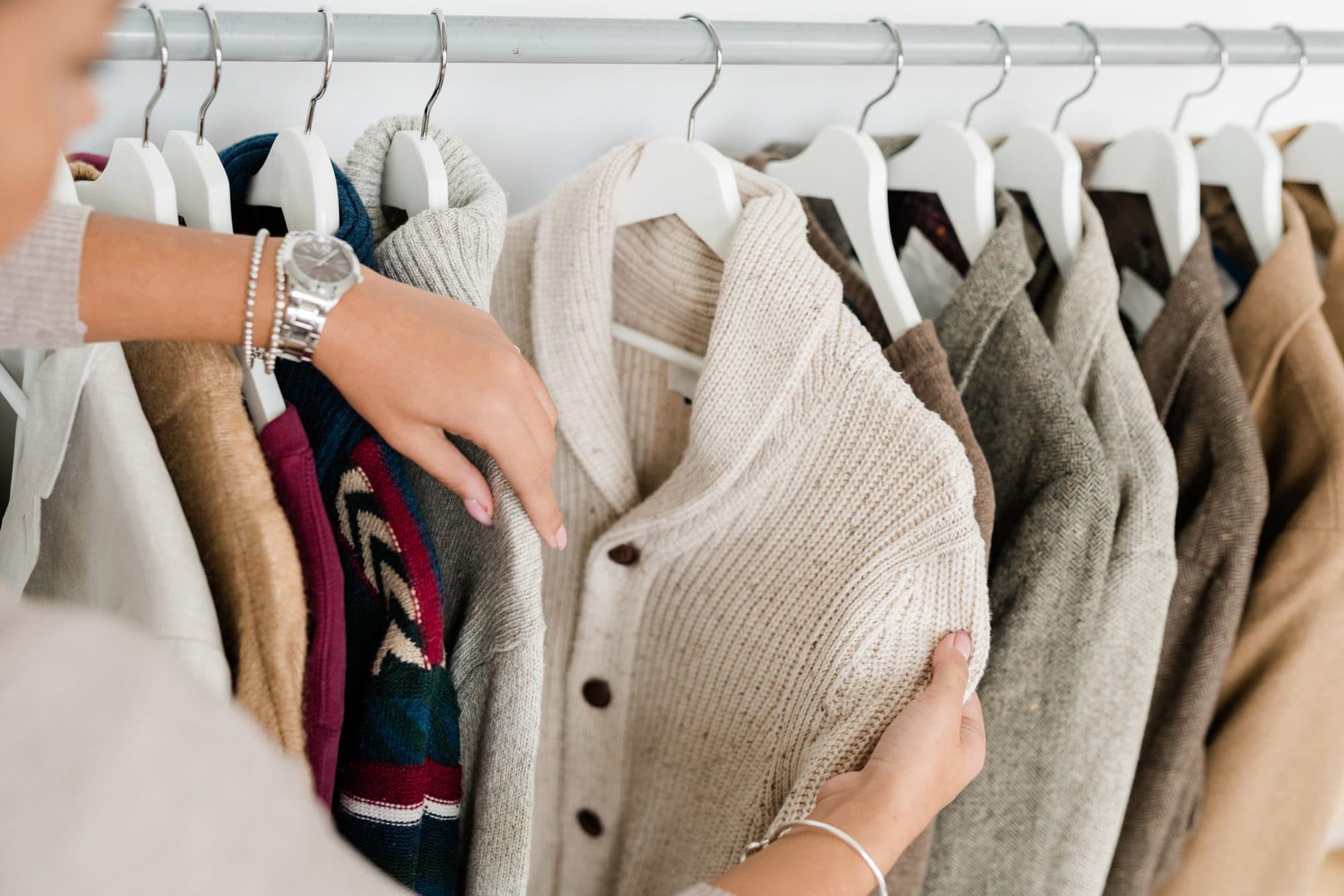 Hands taking a cream cardigan off a clothing rail